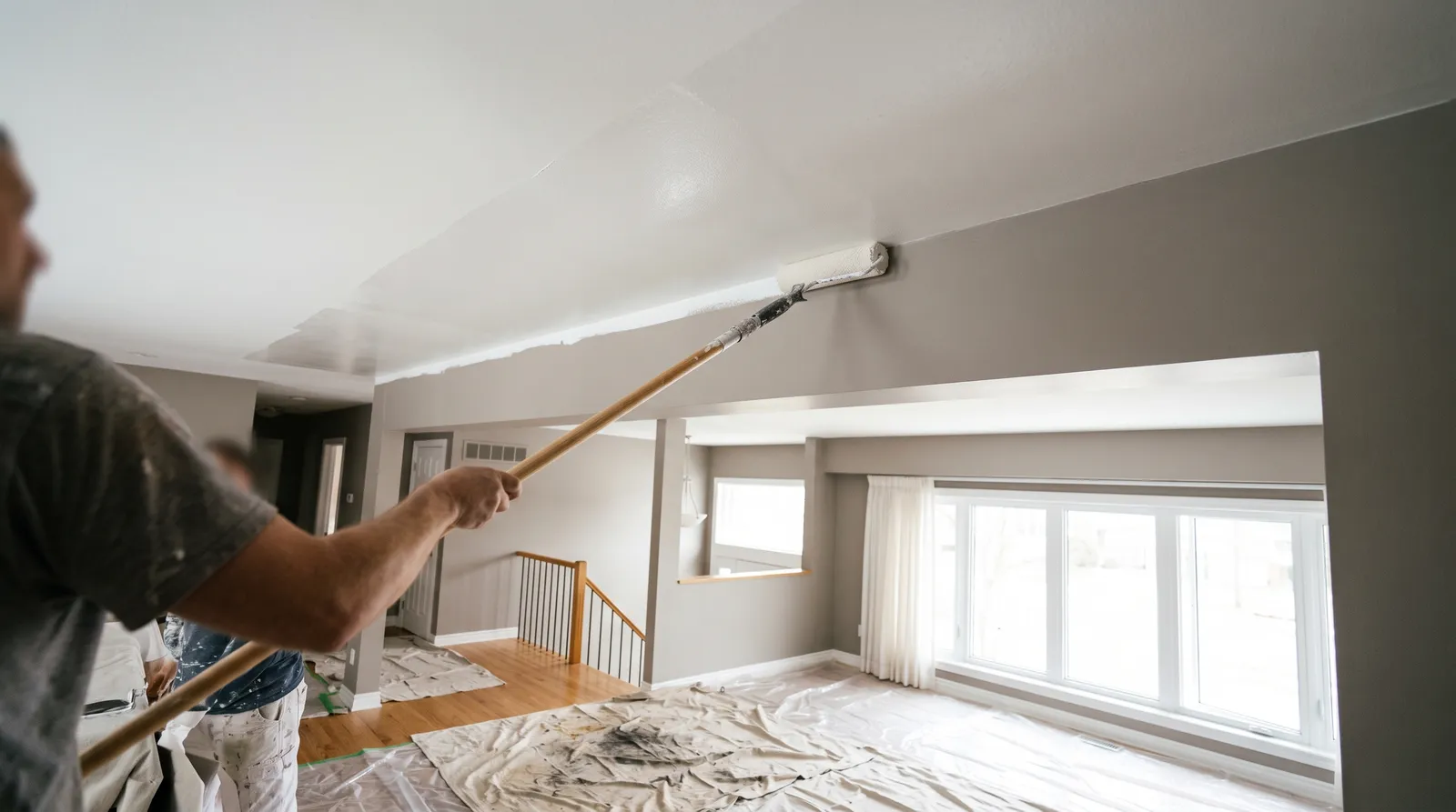 Extension-pole roller laying an even coat of flat white across a smooth ceiling in bright daylight