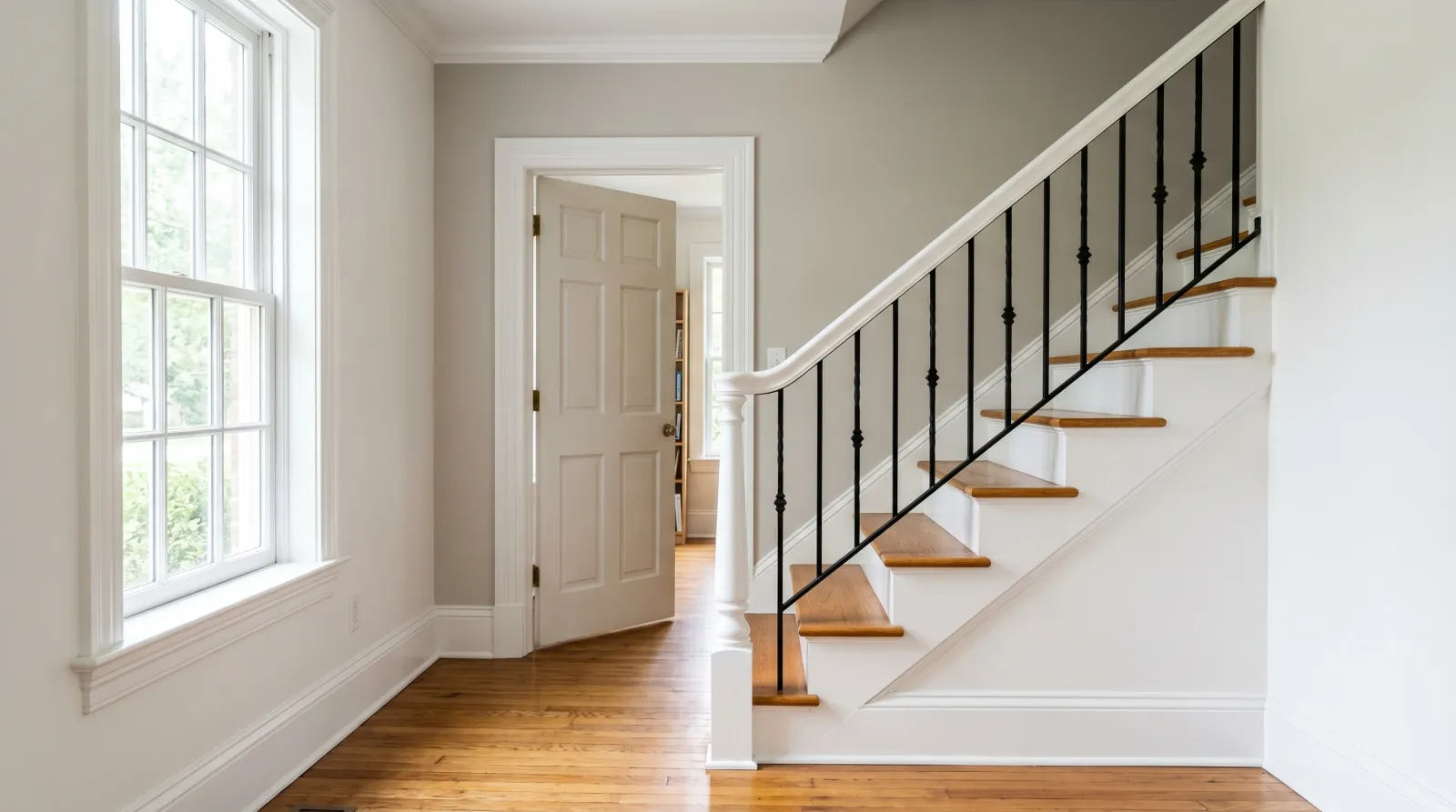Sunlit entry with crisp white semi-gloss trim and a freshly painted black wrought-iron stair railing in soft morning daylight