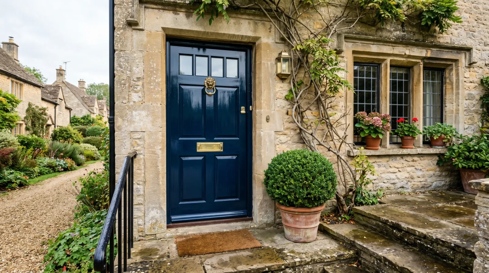 Glossy deep inky-blue front door catching soft morning light, with a brass knocker and a clipped boxwood beside the stone step