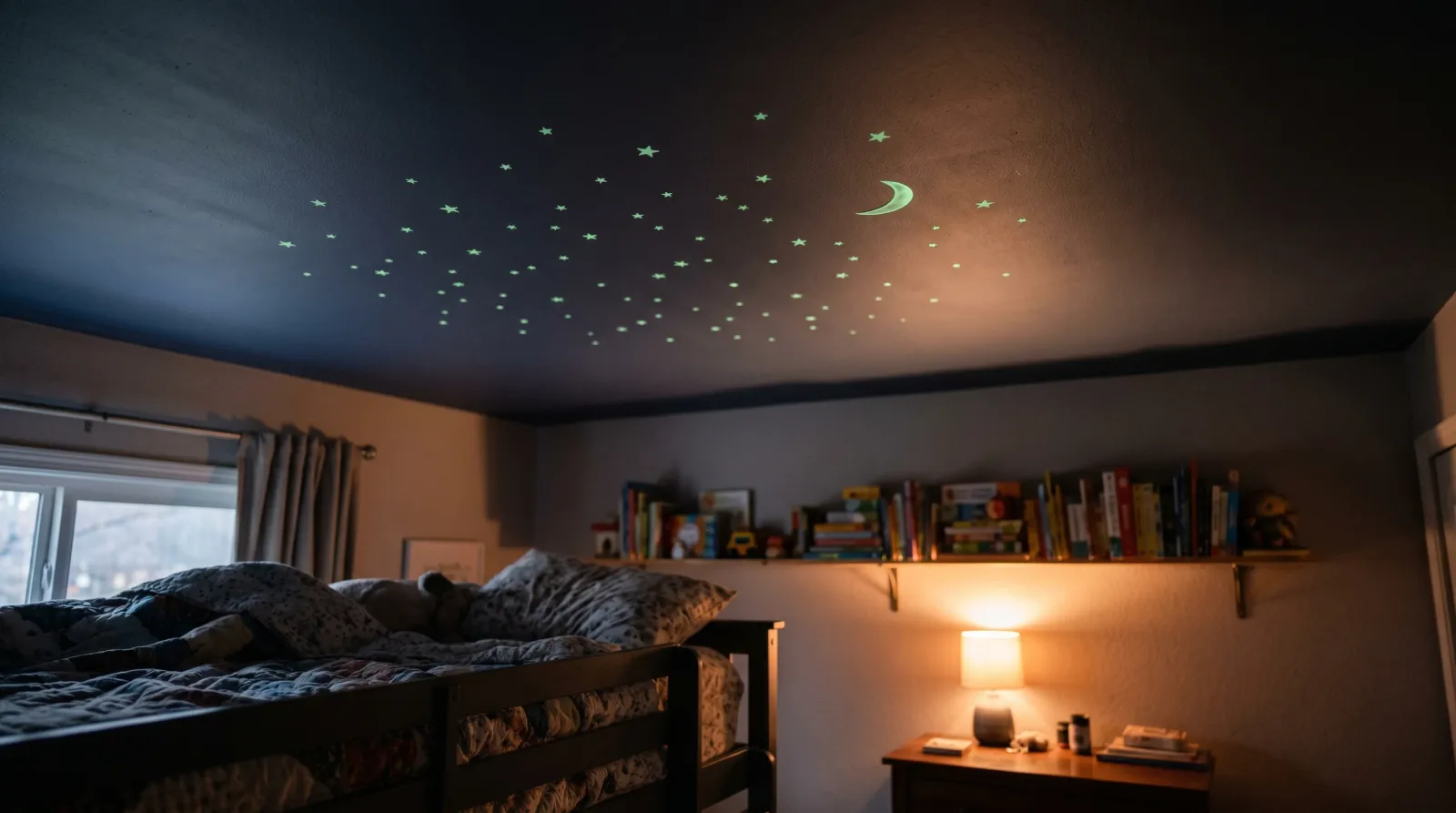 A child's bedroom ceiling at dusk with faint green glowing stars and a thin crescent moon, warm lamplight on the walls below