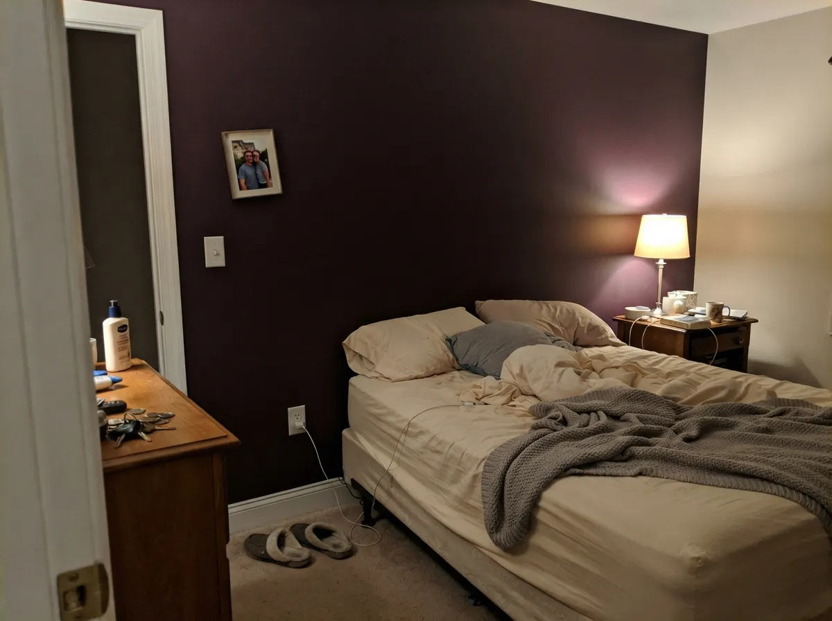 Behind the headboard, under a warm lamp, the wine-red comes forward and the wall goes velvety instead of flat.