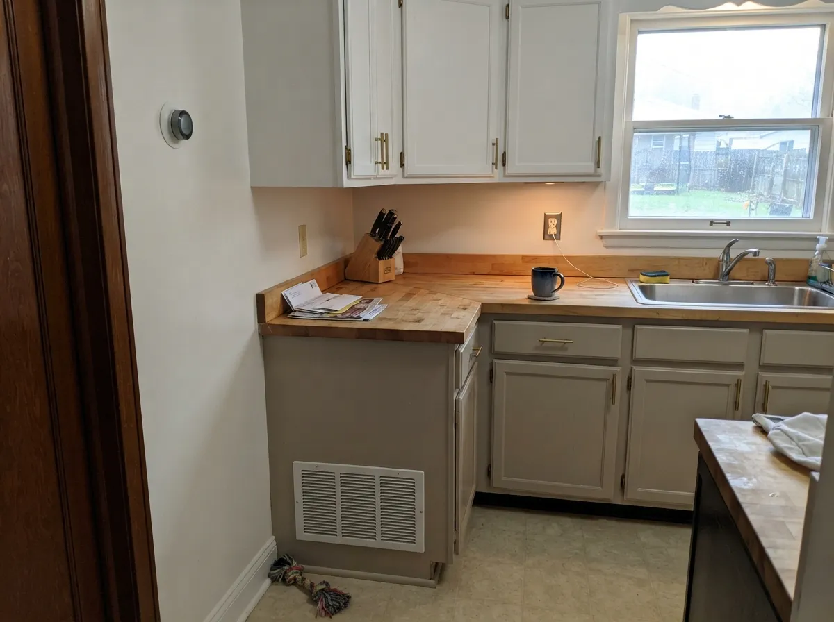 The two-tone kitchen it's built for: greige lowers, white uppers, brass in between.