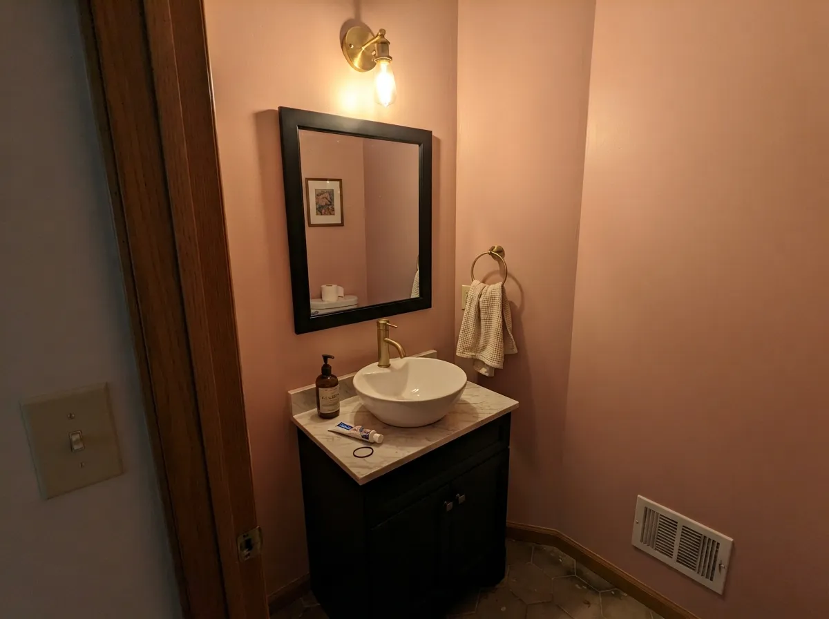 The designer move: a warmly lit powder room where the black vanity and brass faucet keep the pink from feeling delicate.