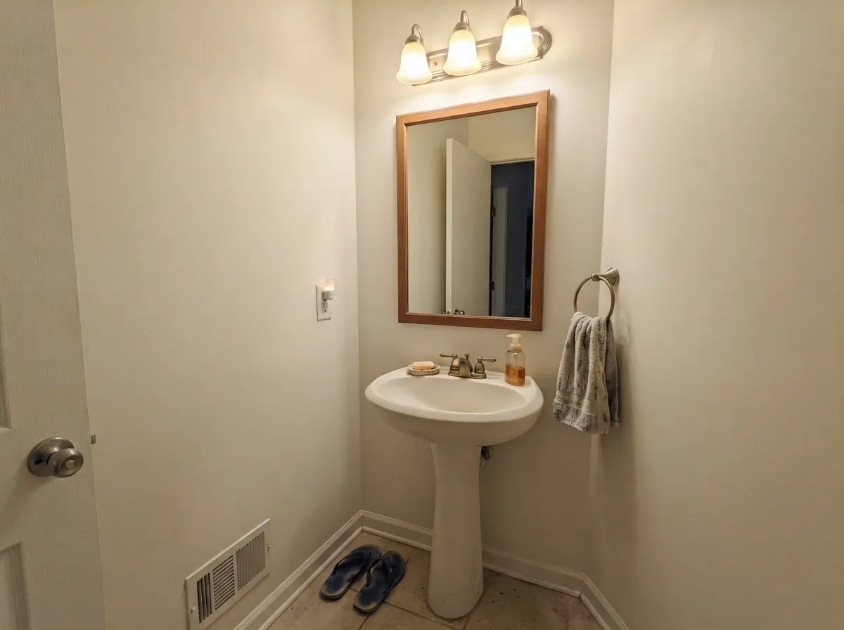 Swiss Coffee walls in a windowless powder room with brass fixtures and warm vanity light.