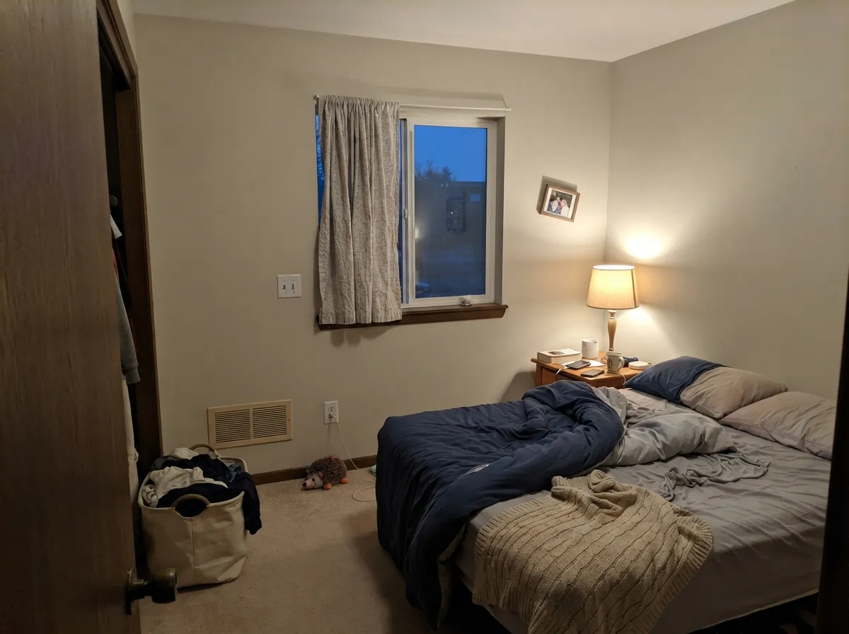 Under warm lamplight in a low-light bedroom, the quiet warmth holds and the room feels calm, not flat.