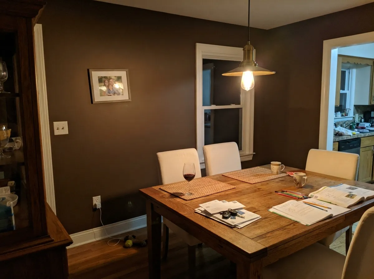 Evening is a dining room's real light, and it is where the red-orange in Kaffee comes forward against cream chairs and brass.