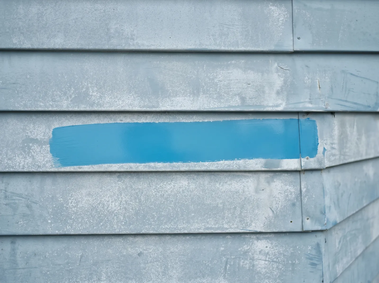 Aluminum siding with one wiped band showing brighter original color against the chalky dull surface