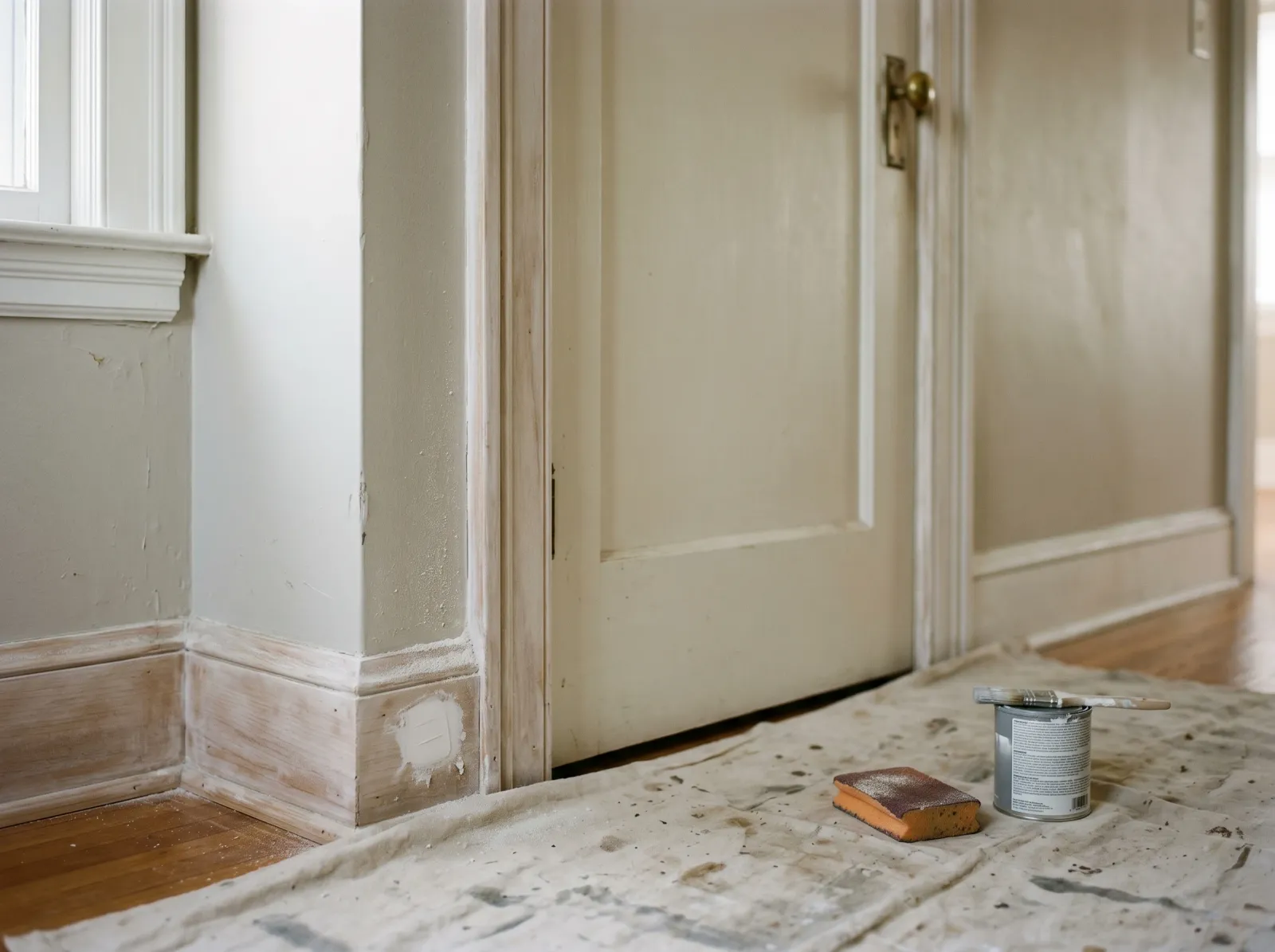 Door frame scuff-sanded and spot-primed, sanding sponge and small can on the drop cloth