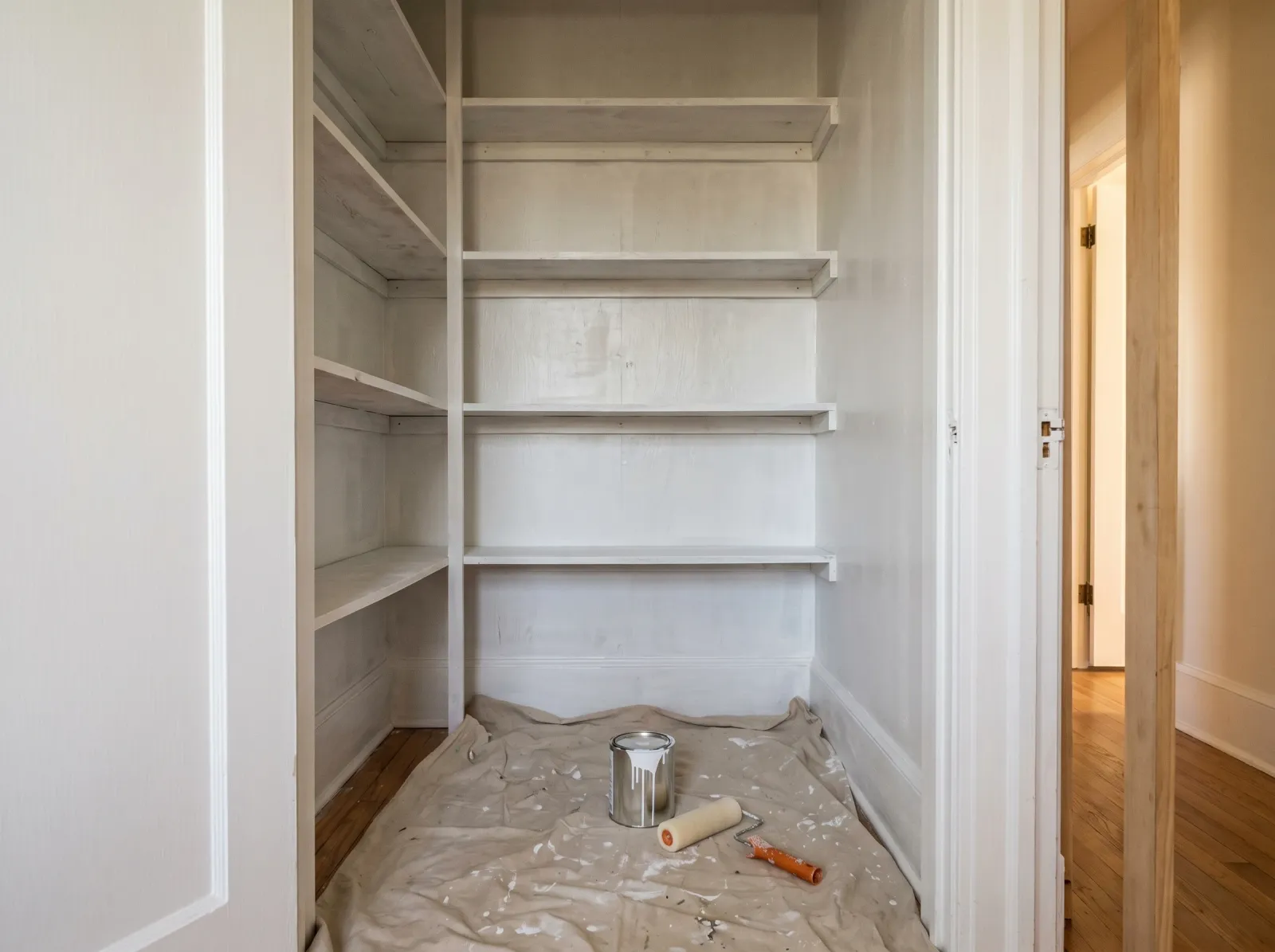 Pantry interior coated in white-grey primer with a mini-roller on the floor